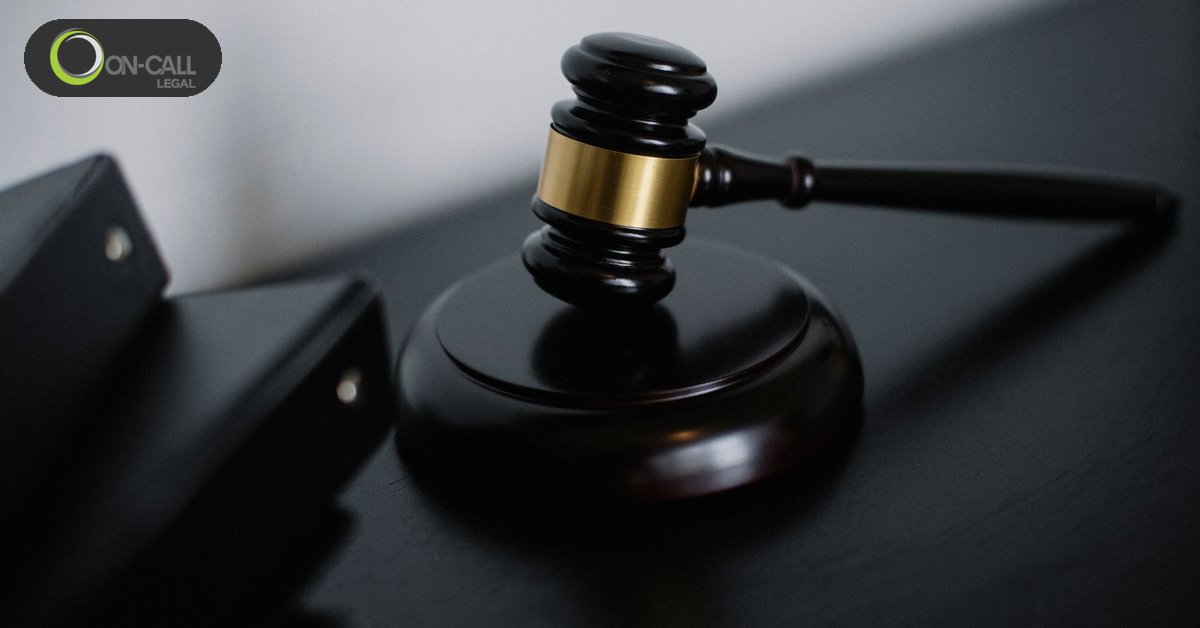 A wooden judge's gavel with a gold band resting on its sound block beside black binders on a dark desk