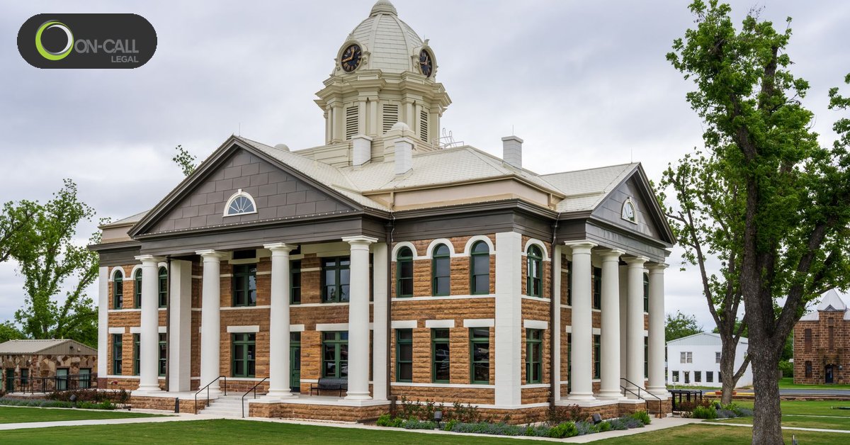 A two-story brick courthouse with white columns and a clock-tower dome under an overcast sky