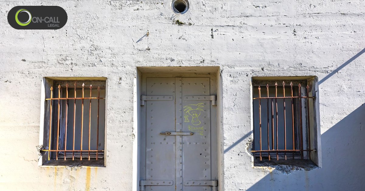 A steel door set between two barred windows in a whitewashed concrete wall