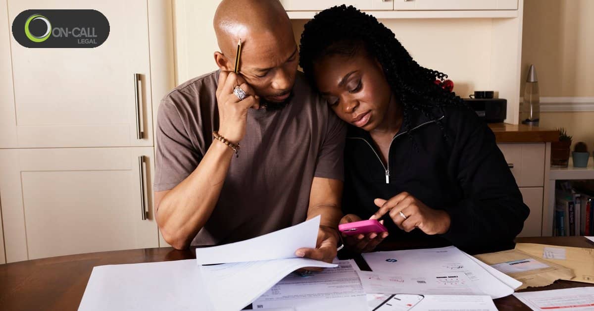 A man and a woman sit close together at a kitchen table reviewing printed statements and a phone