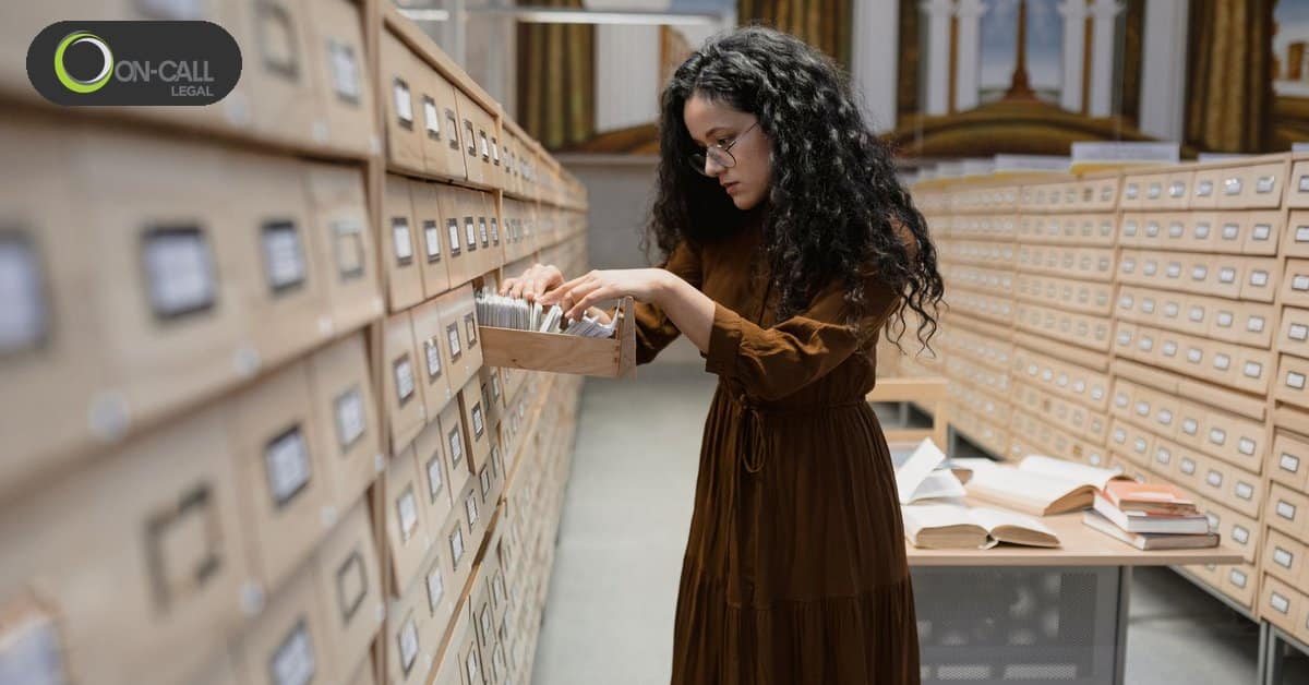 A woman with curly hair looks through an open drawer in a long row of archive file drawers