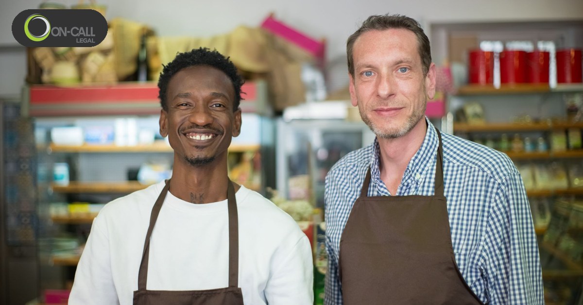 Two shop owners in aprons standing together behind the counter of their store