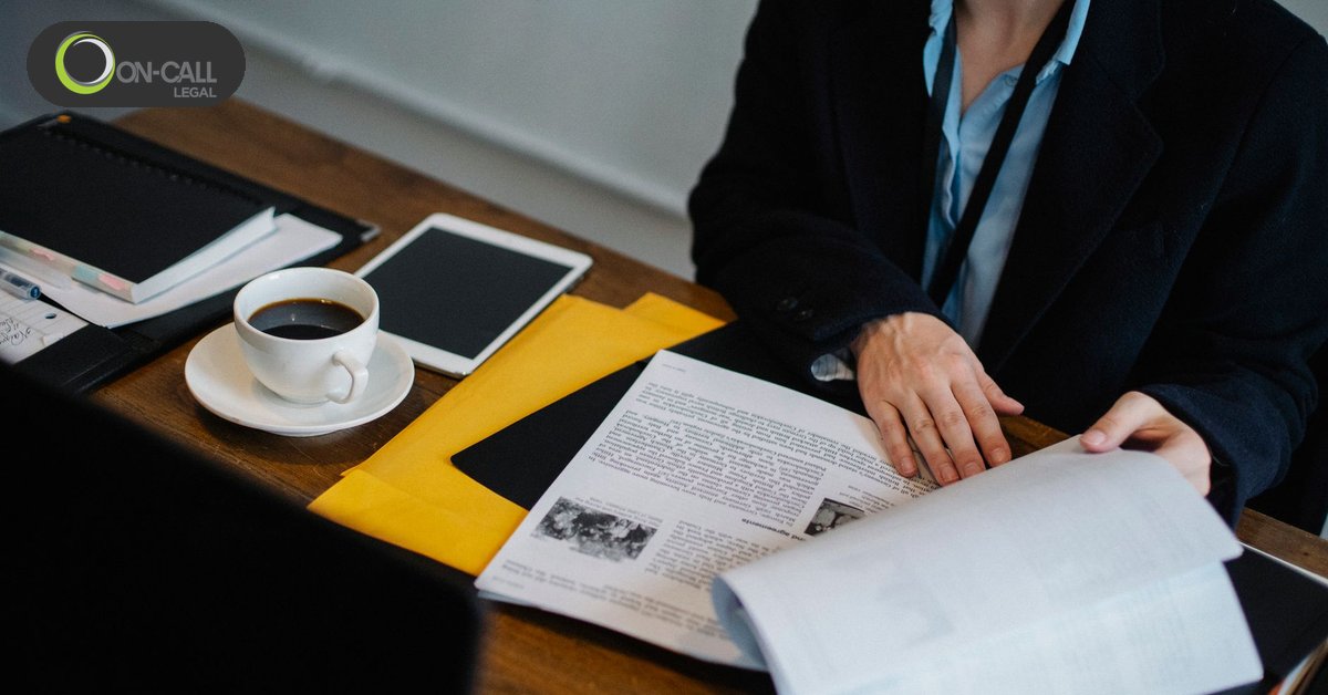 A person in a dark blazer reviews printed documents at a desk beside a tablet and a cup of coffee