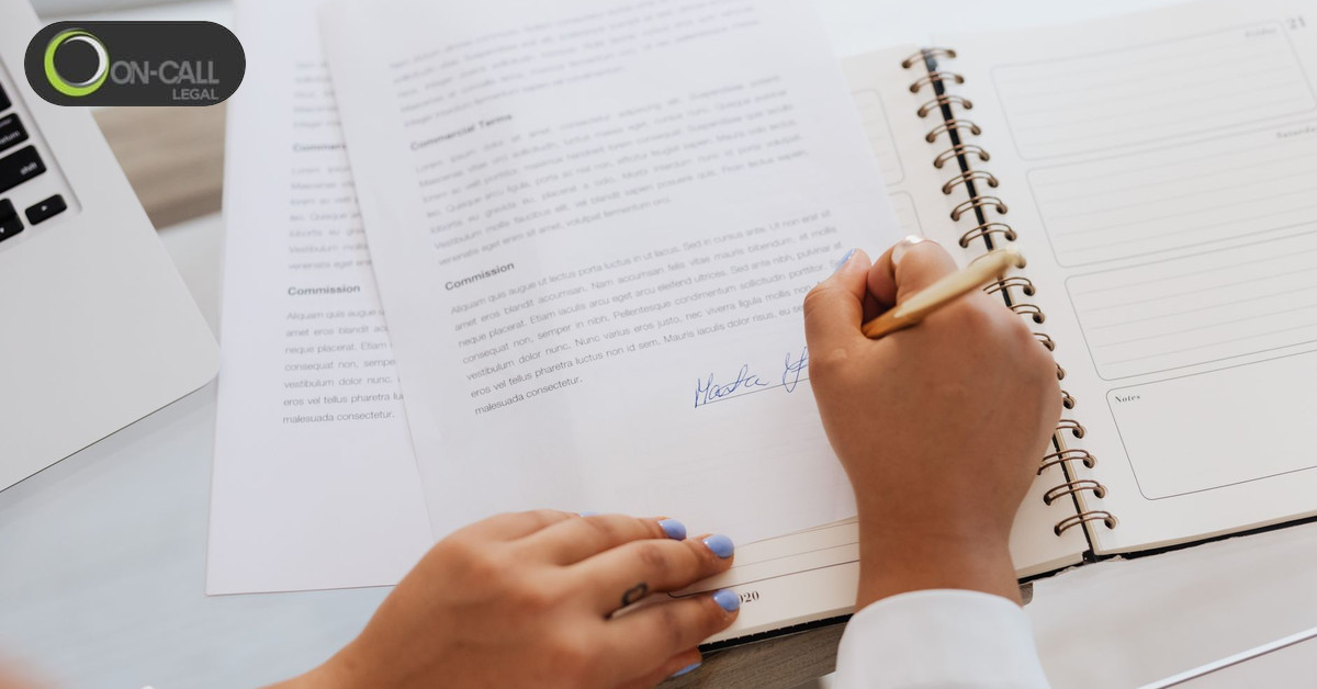 Person signing a printed document beside a laptop and a notebook