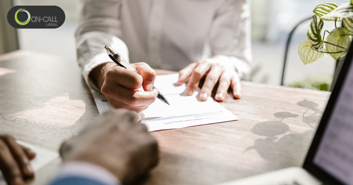 Two people at a desk signing a document, one holding a pen over the page