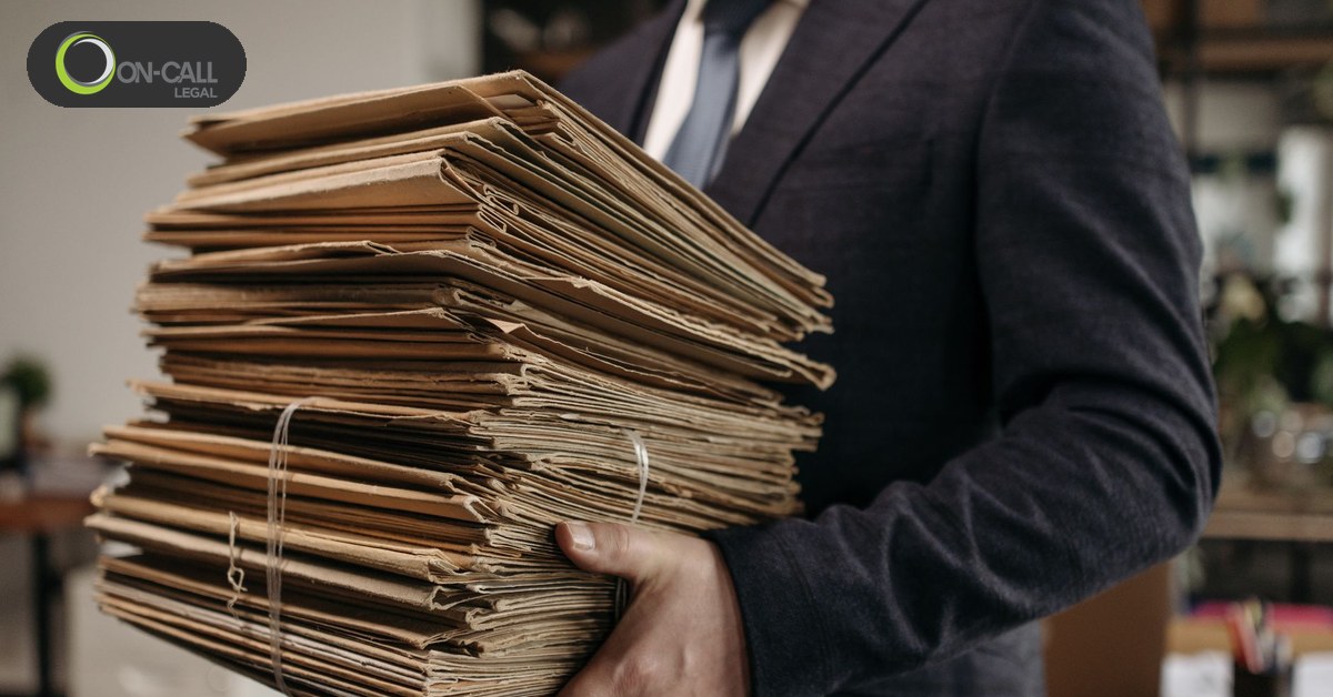 A person in a suit carrying a tall stack of bound case files