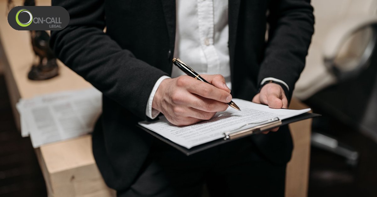 A person in a suit signs a form on a black clipboard with a gold pen