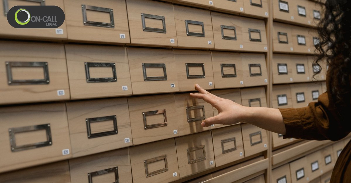 A hand pulling open one drawer in a wall of wooden archive record drawers