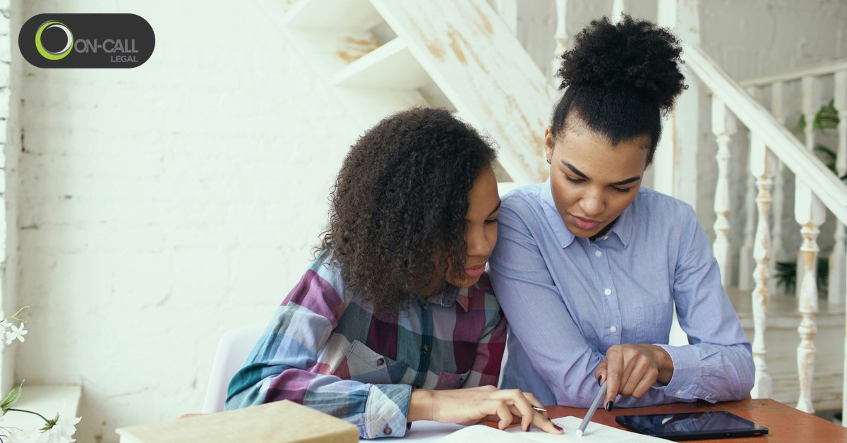 A parent and a teenager sitting together at a table at home, reviewing papers