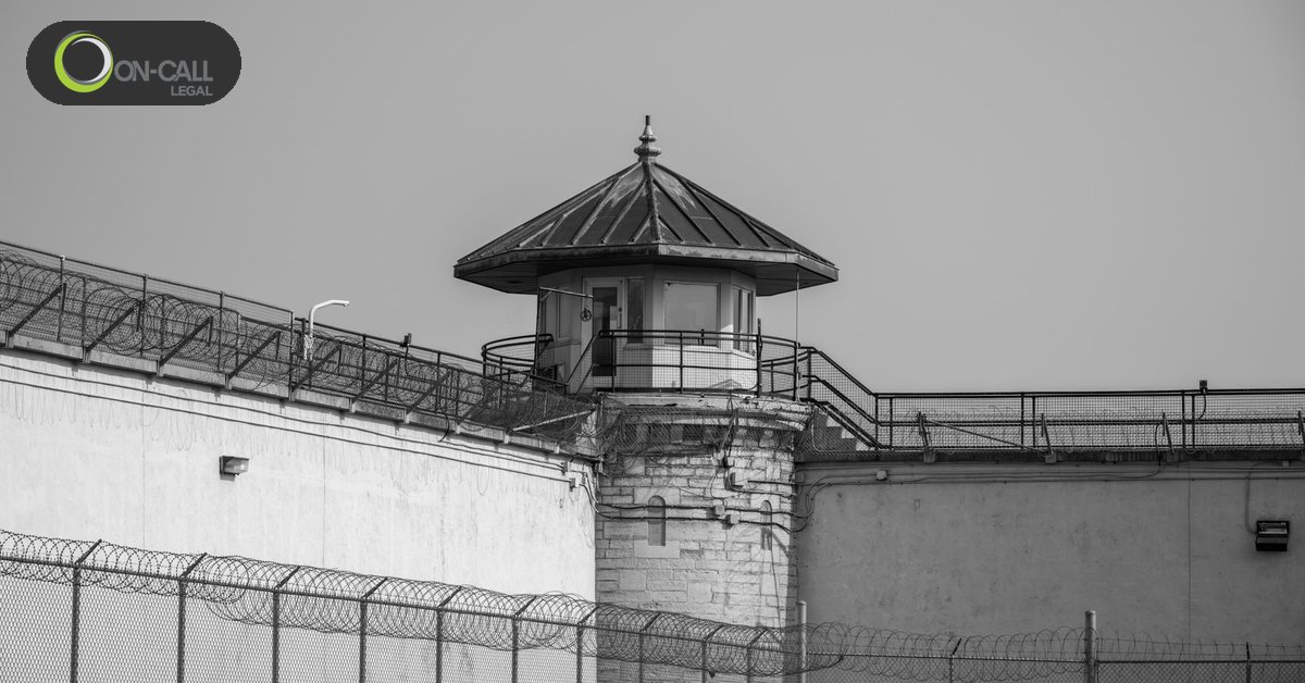 Black-and-white view of a prison guard tower above a razor-wire perimeter fence